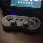 Close-up of a retro-style game controller alongside a modern handheld console on a wooden table.