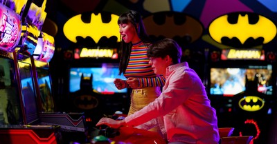 Couple enjoying an arcade gaming night surrounded by neon and Batman decor.