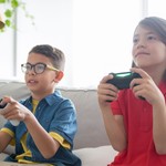 Two kids playing video games on a cozy couch indoors, showcasing fun and technology.