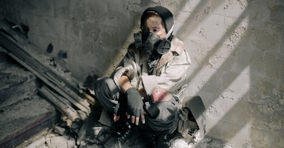 A young person in a gas mask sits in a decaying, abandoned building, evoking themes of survival and desolation.