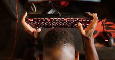Gamer expresses frustration with video game by holding up keyboard. Overhead shot of gaming setup.