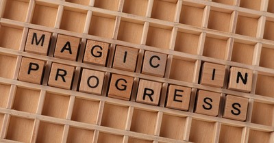 Wooden letter blocks arranged to spell 'Magic in Progress' on a grid.