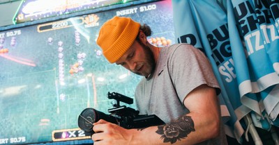 Man with tattoo filming in an arcade, using professional camera equipment.
