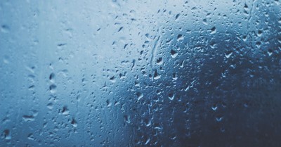 Detailed view of water droplets on a glass window with a blue background.