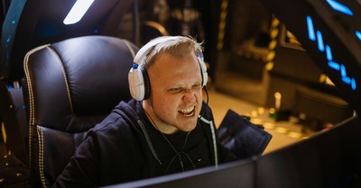 A passionate gamer celebrating victory while gaming indoors with white headphones and a gaming chair.