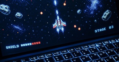 A classic arcade space shooter game displayed on a laptop with illuminated keyboard, showing retro graphics.