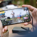 Person playing PUBG on smartphone outdoors with charging cable attached.